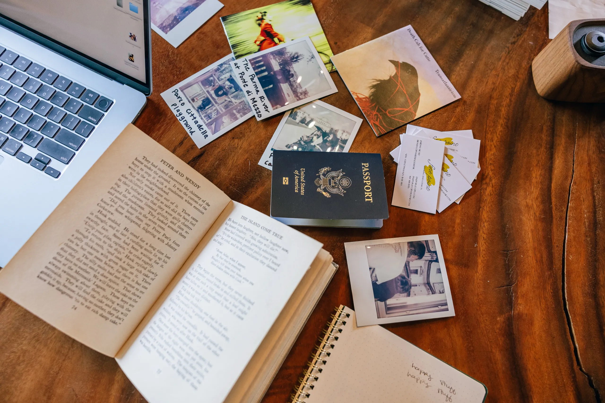 An open book, a passport and scattered polaroid prints on a wooden surface.