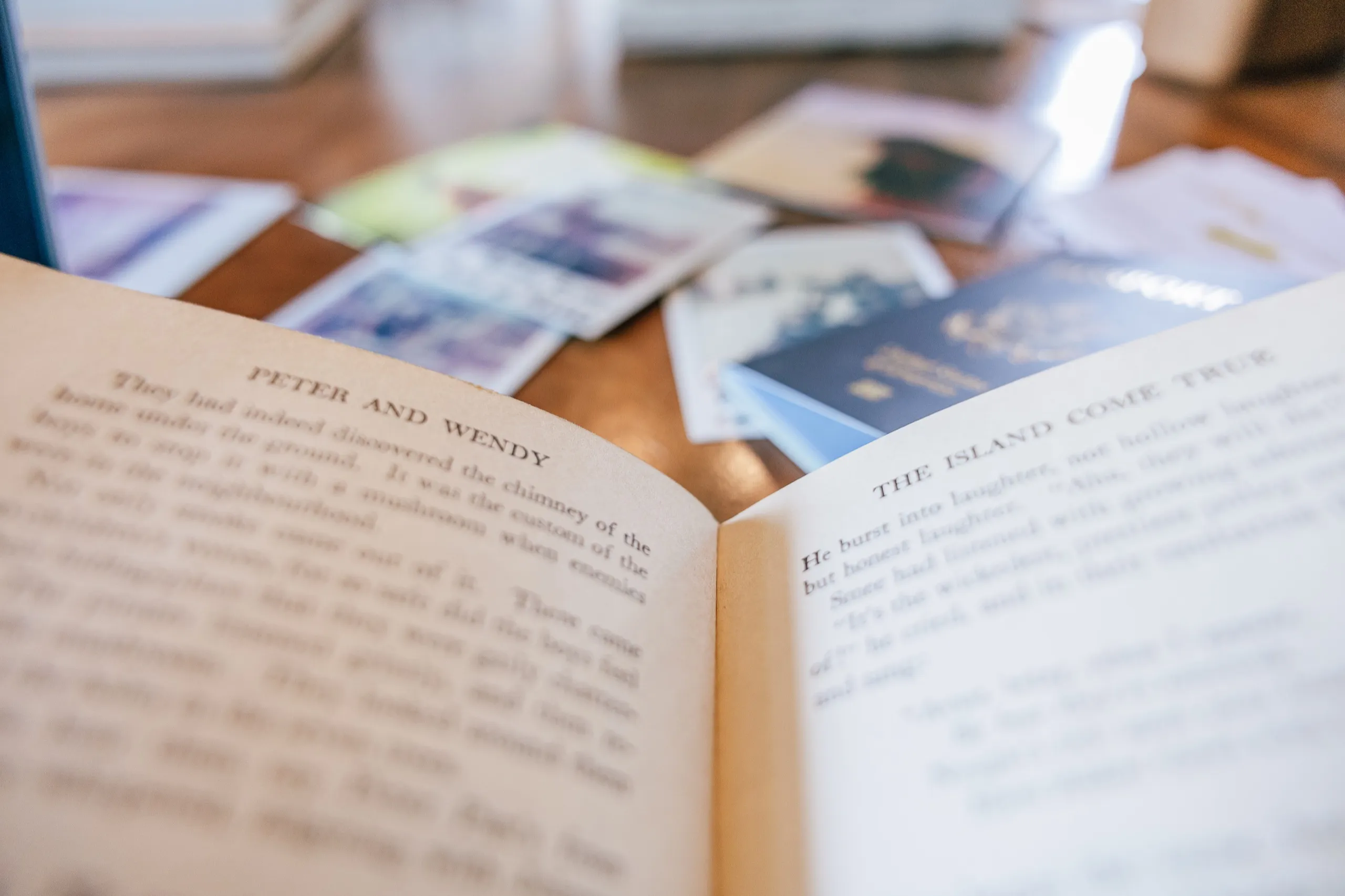 An open vintage book beside travel polaroids on a dark wood table.
