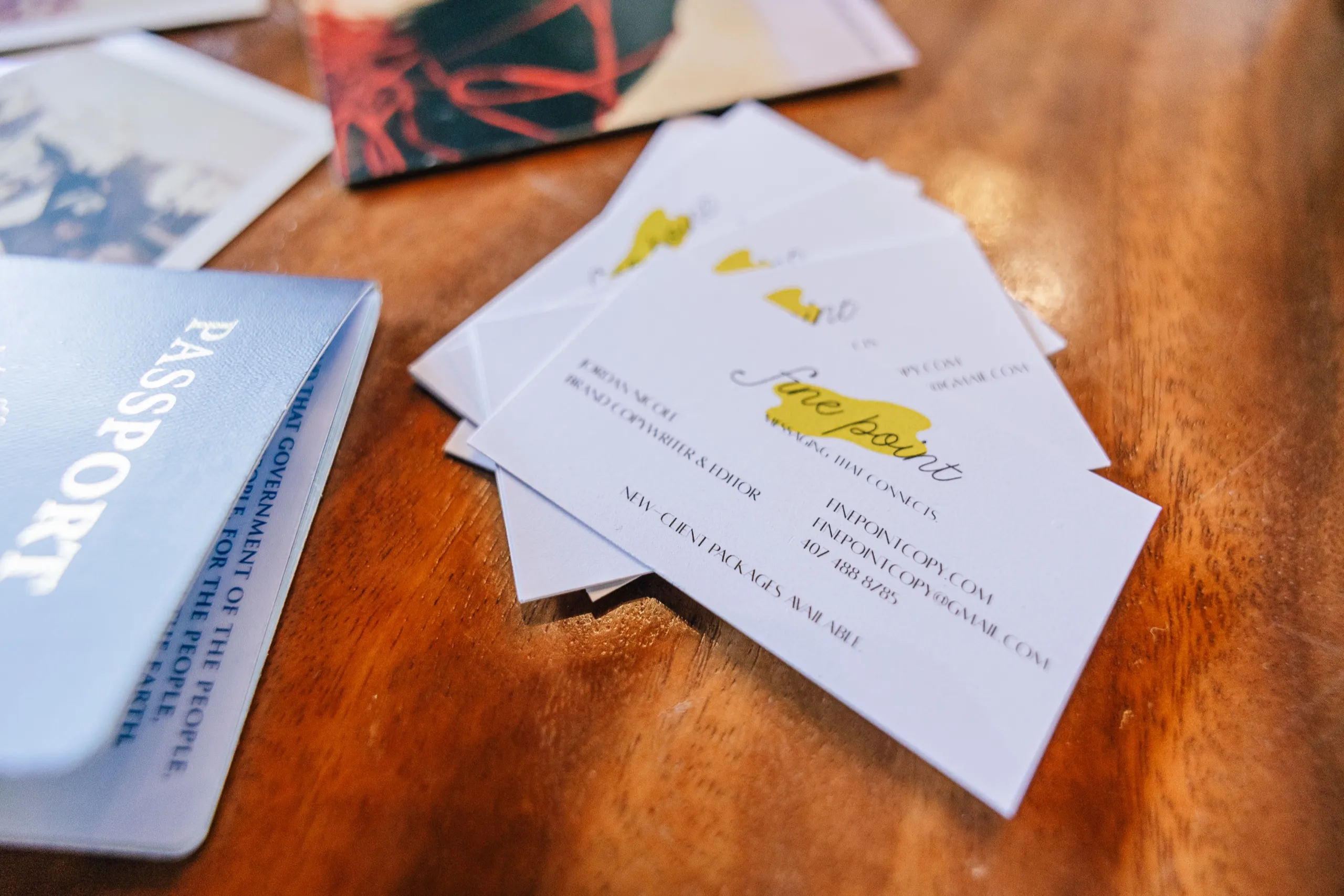 Fine Point business cards fanned across a wooden desk beside a passport.