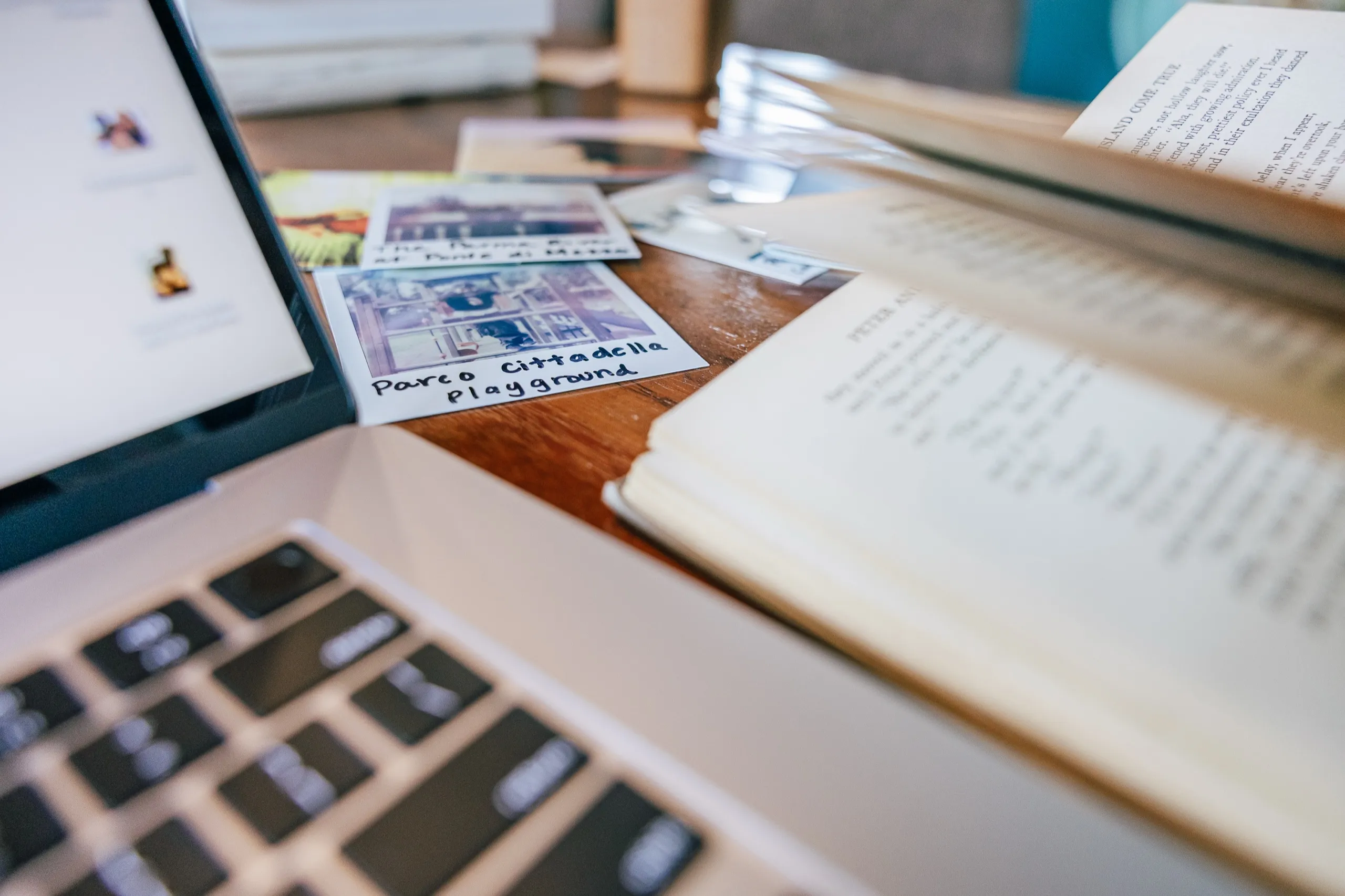 A laptop, an open notebook and printed photographs arranged on a desk.